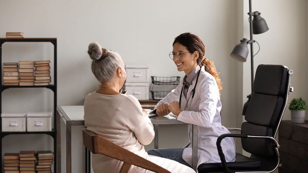 A female doctor is having a conversation with a female patient. They are both sitting in chairs and looking at one another.