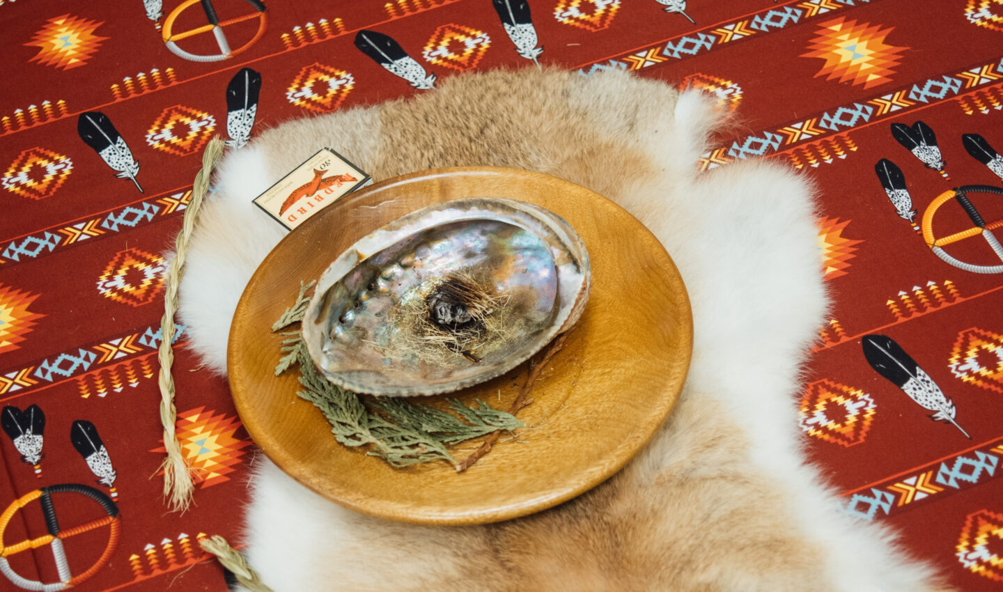 A close up of what's on the circular table in the middle of the room. You see cloth made of rabbit fur and a shell with smudging supplies on top.