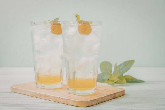 Two tall glasses filled with refreshing citrus mocktail, garnished with a slice of orange and a sprig of mint.