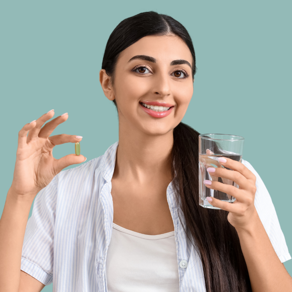 A young woman smiles while holding a pill in one hand and a glass of water in the other.